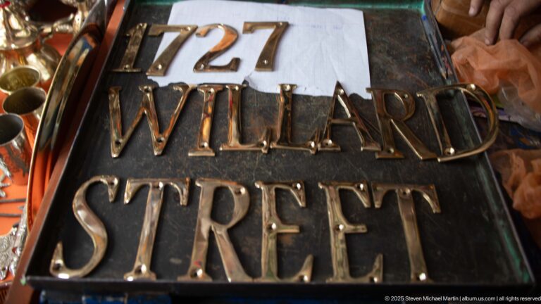 Raised brass-colored letters spelling 727 WILLARD STREET on a dark metal sign surface.