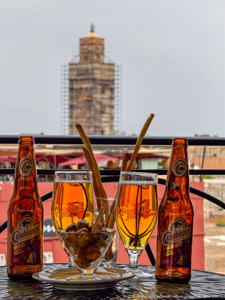 Two Casablanca beer bottles with amber beer in stemmed glasses and a bowl of snacks on a rooftop table.