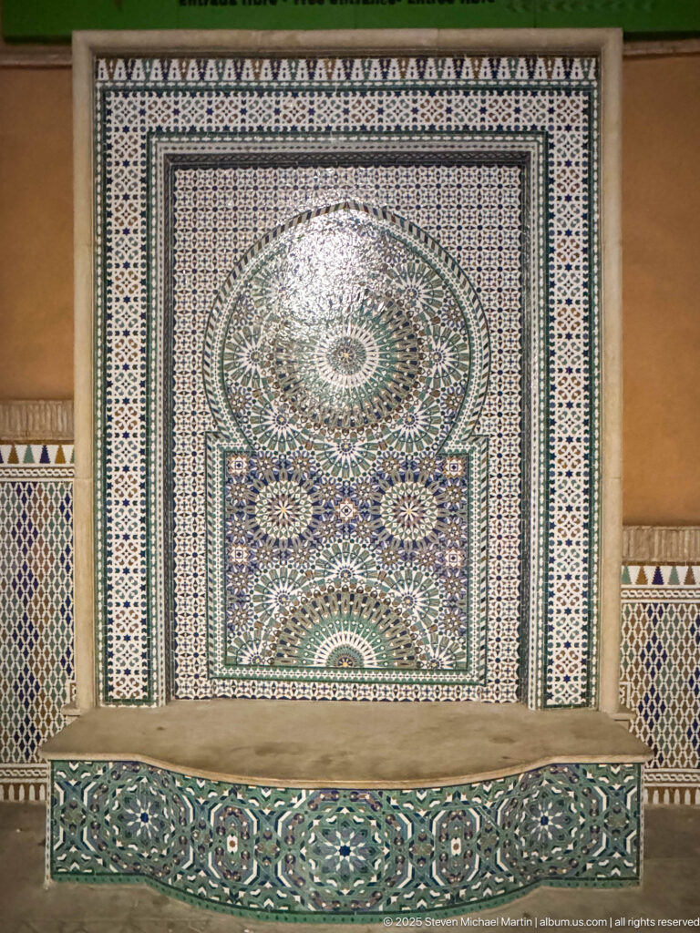 Large Moroccan zellij fountain panel with dense geometric mosaics, central rosette pattern, and tiled basin in Marrakech.