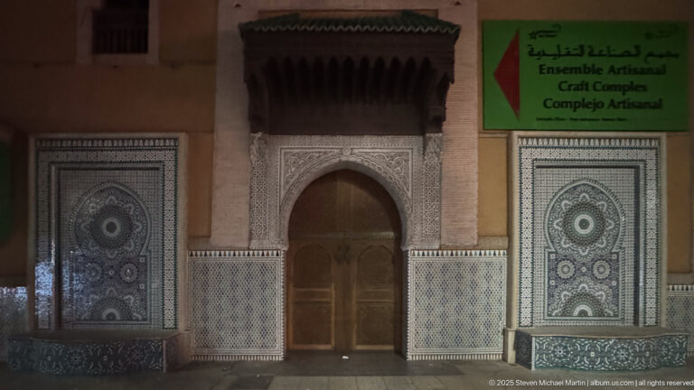 Decorated arched entrance with zellij panels and a green sign identifying the Ensemble Artisanal craft complex in Marrakech.