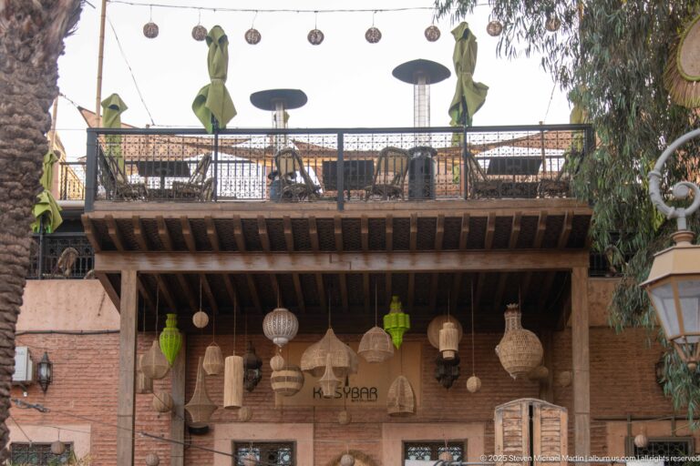 Assorted woven and metal lanterns hanging beneath a timber canopy, with a furnished terrace visible above.