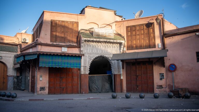 Decorated arched entrance labeled Bahia Souk Artisanal, flanked by wooden shopfronts on a pink Marrakech façade.
