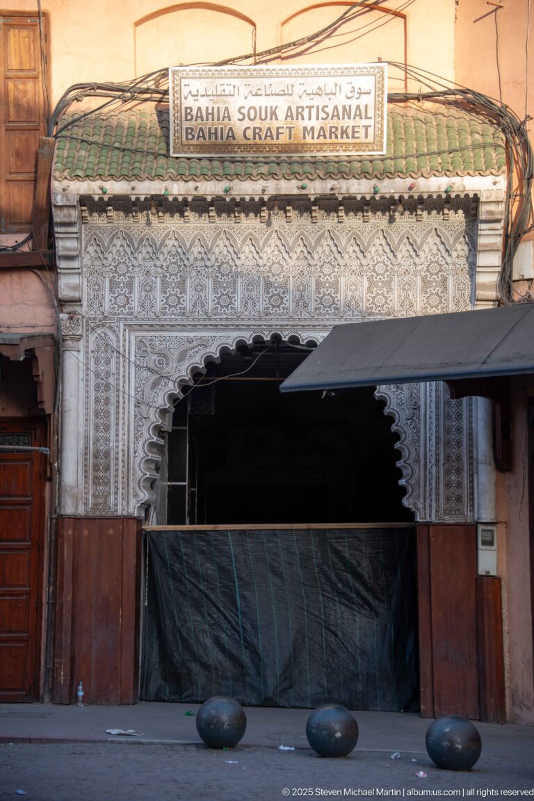Close view of Bahia Souk Artisanal entrance with carved white ornament, scalloped arch, green tile canopy, and dark covering.