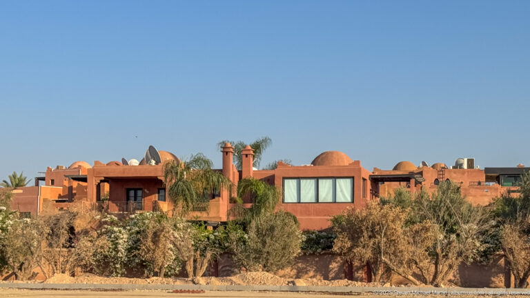 Terracotta villas with palms, olive trees, roof terraces, and projecting chimney-like towers in Marrakech.