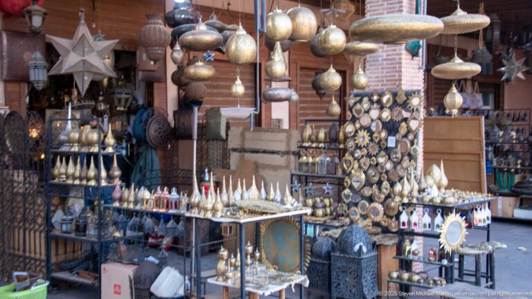 Marrakech shopfront crowded with hanging metal lanterns, mirrors, trays, bottles, and decorative craft objects.