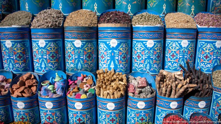 Blue patterned market tins filled with dried herbs, flowers, roots, bark, and other aromatic goods in Marrakech.