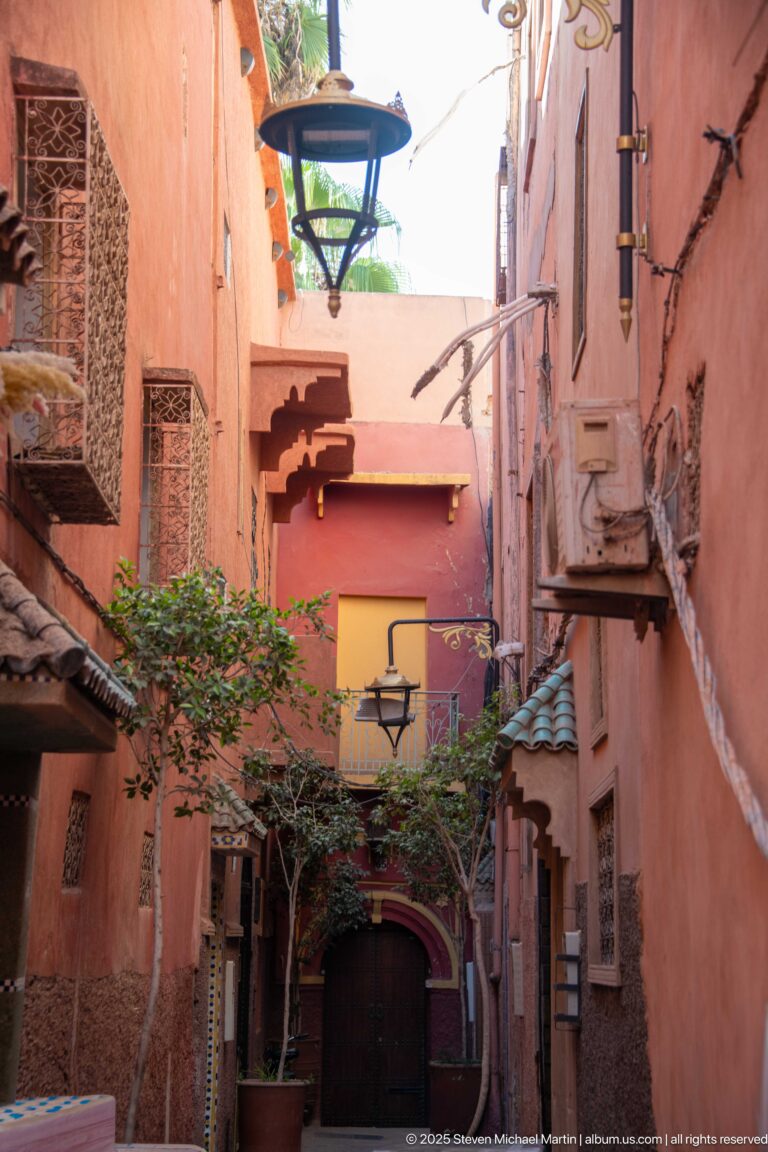 Narrow pink-walled courtyard with balconies, vines, carved screens, air-conditioning units, and a large hanging metal lantern.