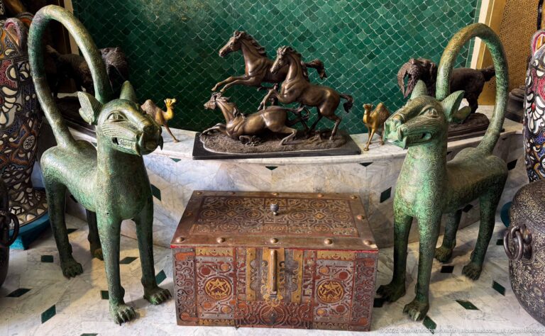 Two green horned animal sculptures beside an ornate inlaid chest, with equestrian and animal figures displayed behind.