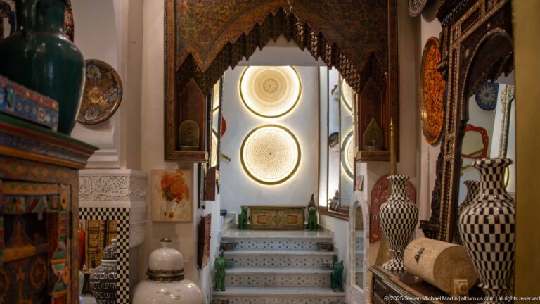Short white stair beneath two glowing circular panels, framed by a carved dark wooden arch and large patterned ceramic vessels.