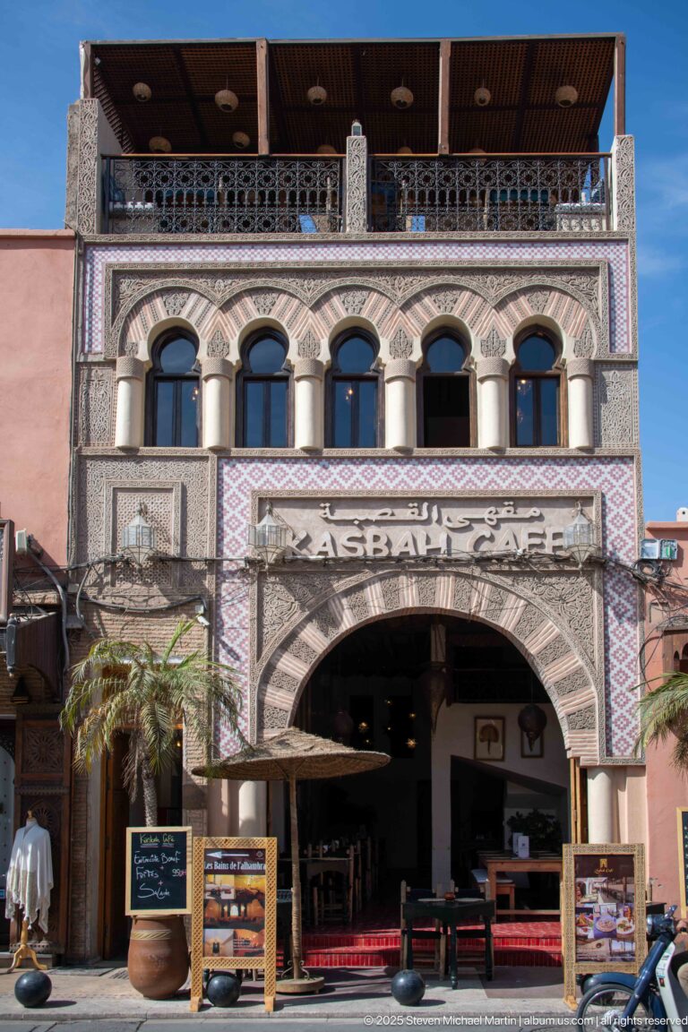 Kasbah Café façade with large entrance arch, horseshoe-arched upper windows, patterned tilework, rooftop terrace, and menu boards.