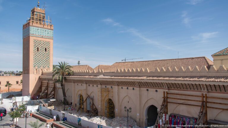 Elevated view of Koutoubia Mosque with its square minaret, tiled roofs, scaffolding, and conservation work along the exterior.