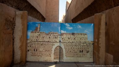Large reconstruction panel showing an intact arched doorway positioned between surviving earthen walls at Badii Palace.