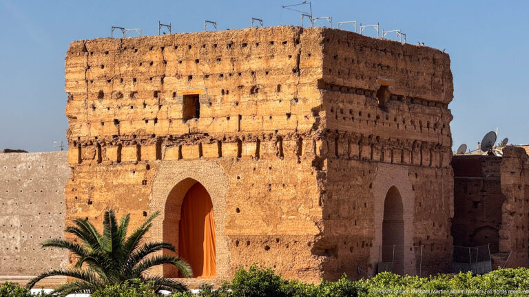 Massive square earthen pavilion with tall arched openings and a palm tree in the gardens of Badii Palace.