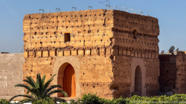Massive square earthen pavilion with tall arched openings and a palm tree in the gardens of Badii Palace.