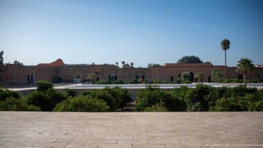 Wide view across the landscaped interior of Badii Palace toward low palace walls, pavilions, palms, and paved paths.
