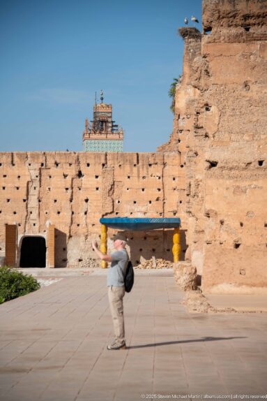 Visitor walking across a broad paved court beside high eroded earthen walls inside Badii Palace.