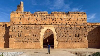 Visitor standing beneath a large pointed arch in a perforated, weathered earthen wall at Badii Palace.