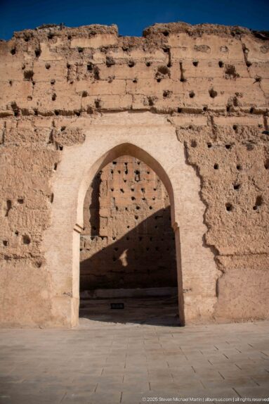 Pointed arch passage outlined in pale masonry within a heavily eroded earthen wall at Badii Palace.