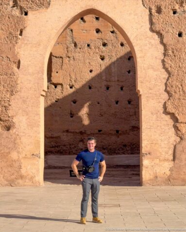Visitor standing beneath a tall pointed arch in a weathered earthen wall at Badii Palace.