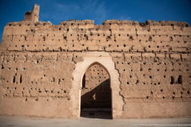 Pointed arched doorway outlined in pale masonry within a broad, weathered earthen wall at Badii Palace.