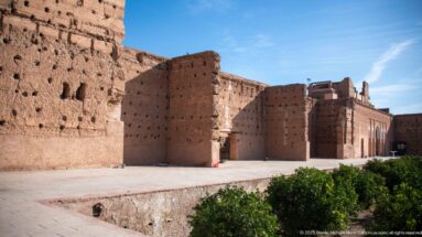 Layered view of massive earthen walls, openings, paved courts, and low greenery inside the Badii Palace ruins.