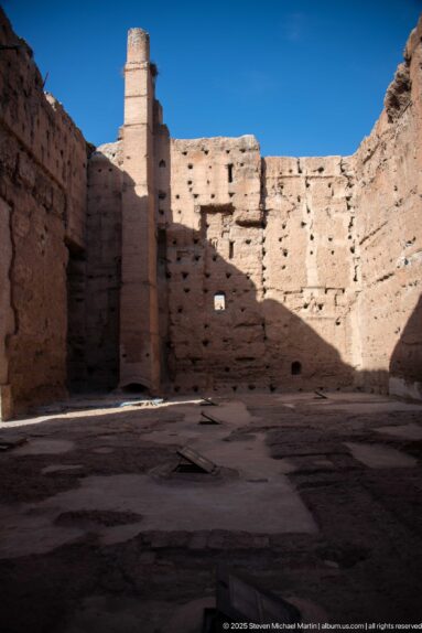Shadowed interior court at Badii Palace enclosed by tall weathered earthen walls with sunlit upper sections.
