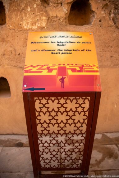 Orange and red multilingual safety sign at Badii Palace warning visitors not to climb the walls.