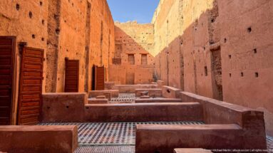 Sunlit Badii Palace interior with repeated low walls, colorful geometric tile floors, and tall wooden shutters.