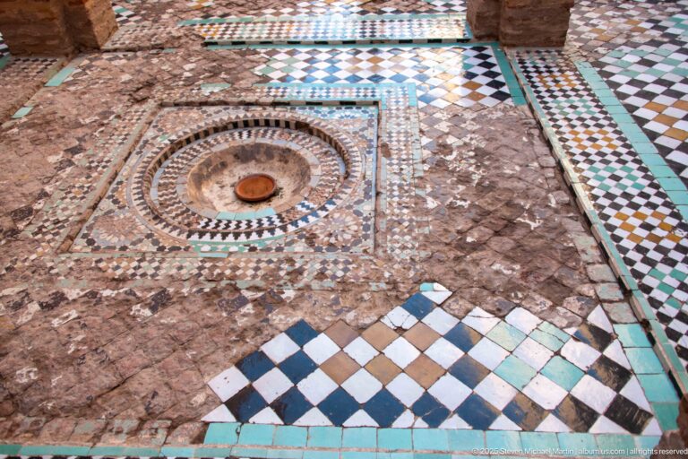 Geometric zellij floor at Badii Palace surrounding a small circular basin, with worn and missing tile areas.