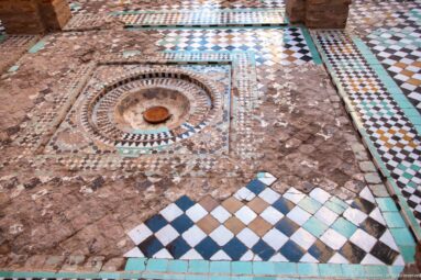 Geometric zellij floor at Badii Palace surrounding a small circular basin, with worn and missing tile areas.