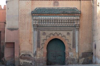 Close view of a green arched double door with carved decoration, patterned bands, and a green-tiled canopy in Marrakech.