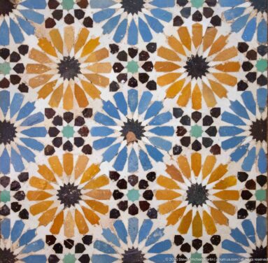 Close-up of Moroccan zellij with repeated ochre and blue starbursts formed from green, white, and dark geometric tile pieces.