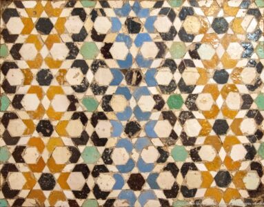 Close-up of worn multicolored zellij made from interlocking stars, polygons, and cream-colored angular tile pieces.