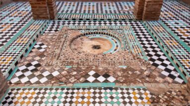 Wide view of a circular basin set within worn geometric zellij paving and low masonry elements at Badii Palace.
