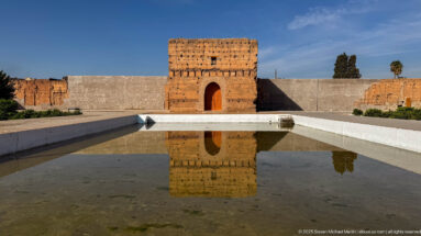 Rectangular earthen pavilion with a tall arched doorway reflected in a shallow basin at Badii Palace.