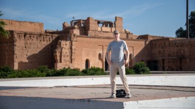 Visitor standing before a reddish Badii Palace façade with a large central doorway and smaller arched openings.
