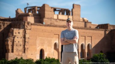 Close portrait of a visitor with the reddish arched ruins of Badii Palace softly blurred behind him.