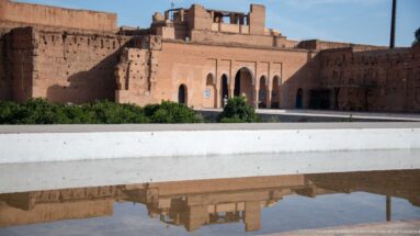 Reddish arcaded Badii Palace façade and upper ruins reflected in a long rectangular basin.