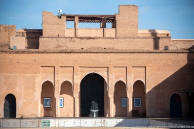 Reddish Badii Palace façade with a broad central arch, four narrower arches, and a small fountain centered in front.