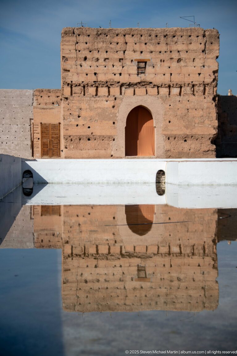 Small arched doorway in a low weathered Badii Palace wall reflected clearly in a shallow basin.