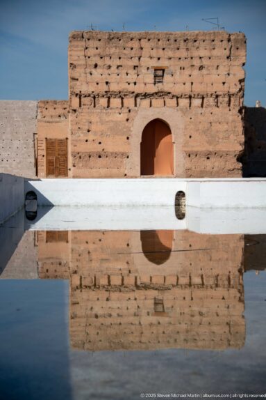 Small arched doorway in a low weathered Badii Palace wall reflected clearly in a shallow basin.