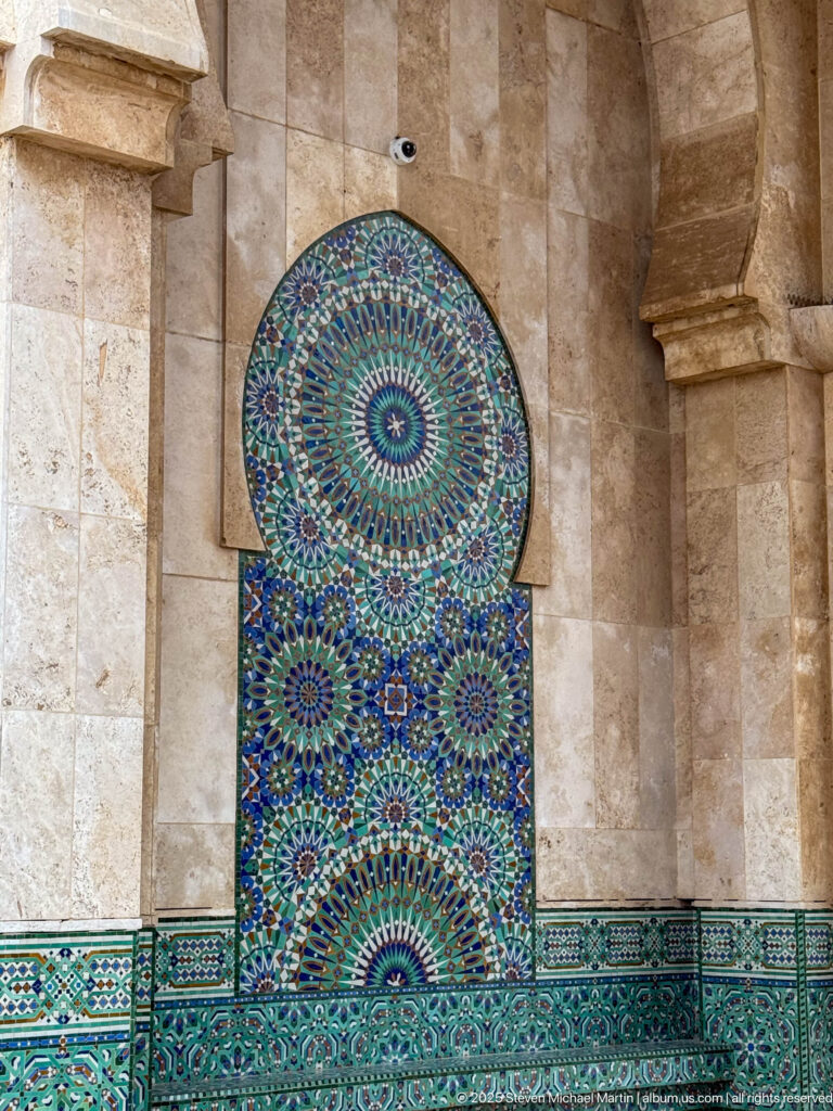 Colorful geometric zellij tile panel set in an arched recess above a matching tiled dado near the Badii Palace entrance.