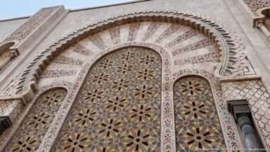 Upward view of a carved horseshoe arch filled with repeating geometric patterns and framed by ornate pale stonework.