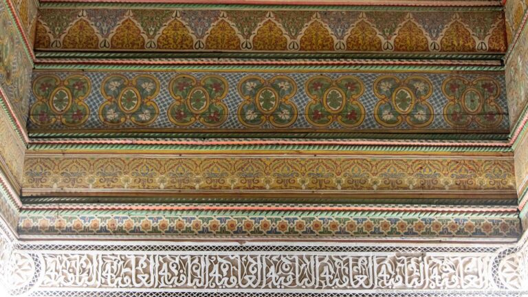Painted green-and-ochre decorative bands above a pale carved Arabic calligraphic frieze at Bahia Palace.