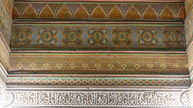 Painted green-and-ochre decorative bands above a pale carved Arabic calligraphic frieze at Bahia Palace.