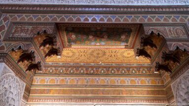 Polychrome Bahia Palace wooden canopy with carved brackets, floral underside and pale plaster supports.