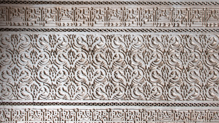 Close Bahia Palace stucco panel with dense vegetal arabesque carving between two Arabic calligraphic bands.