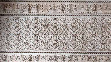 Close Bahia Palace stucco panel with dense vegetal arabesque carving between two Arabic calligraphic bands.