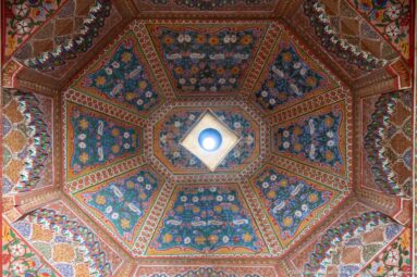 Octagonal Bahia Palace painted ceiling radiating from a central light opening through eight richly patterned panels.