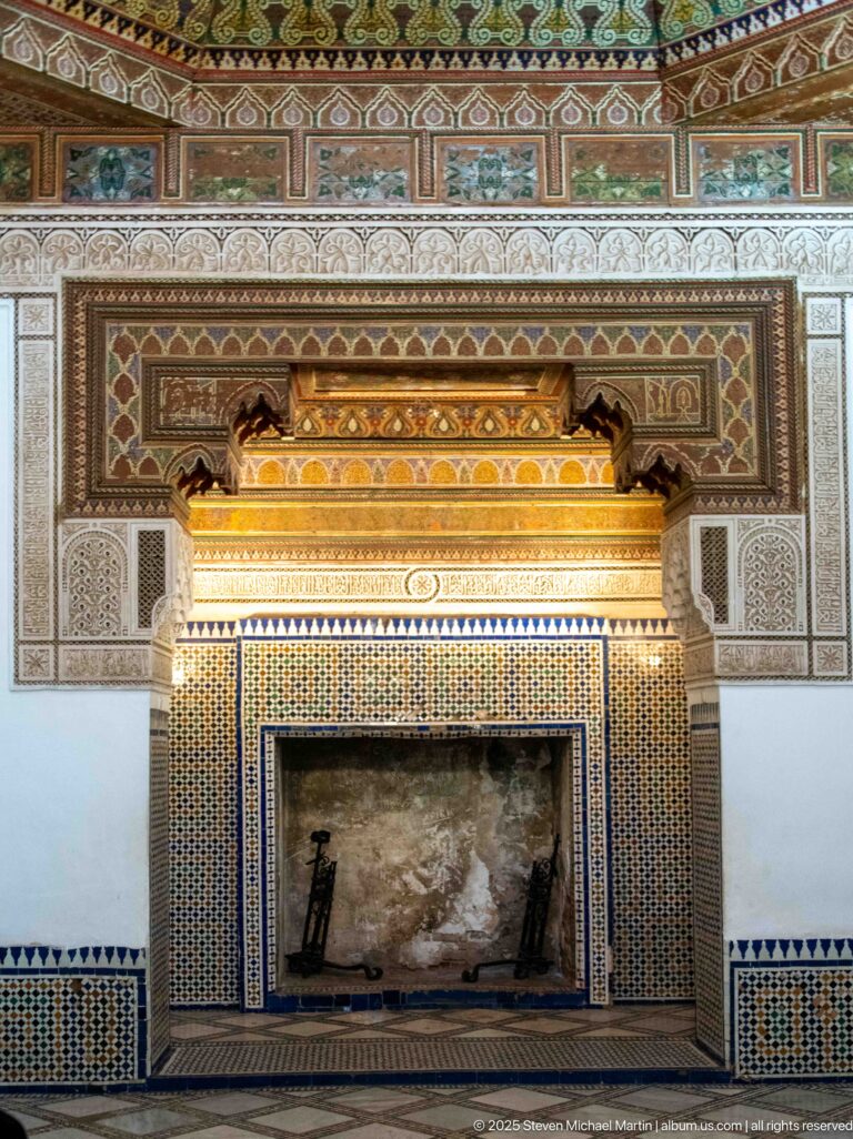 Large Bahia Palace fireplace with dark hearth, geometric zellij, carved plaster panels and projecting golden-toned hood.